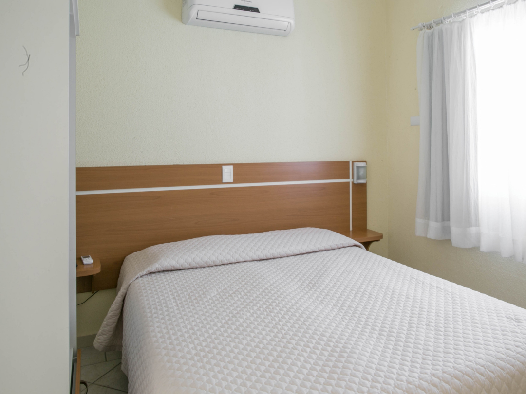 Foto do quarto do apartamento família com cozinha e varanda no Bombinhas Praia Apart Hotel II mostrando a cama e o ar condicionado.